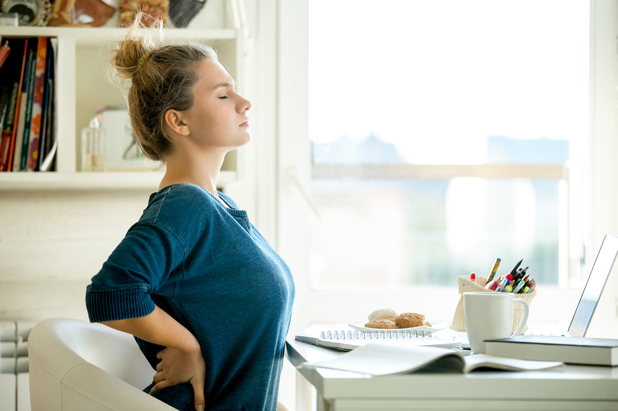 Portrait d'une jolie femme sur une chaise à la table avec une tasse et un ordinateur portable, un livre, des crayons, un cahier dessus.